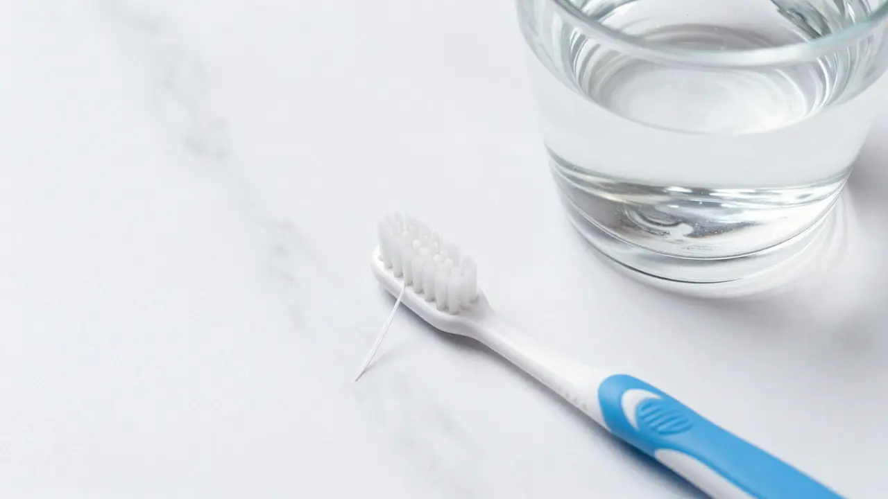 Mezizubní kartáček, dentální nit a sklenice vody jako symboly správné hygieny.